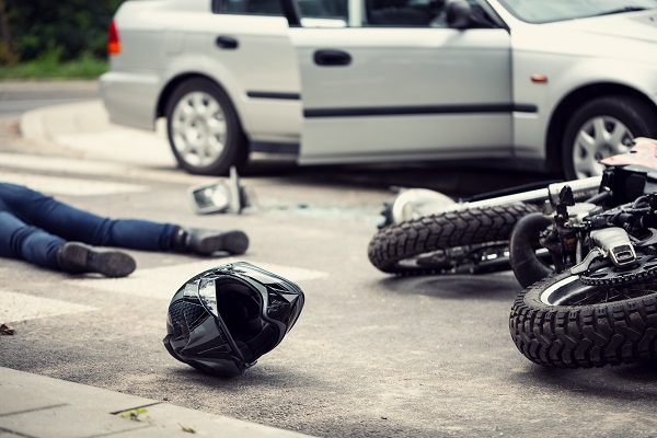 A biker is on the ground next to a black helmet and motorcycle after getting hit by a car.