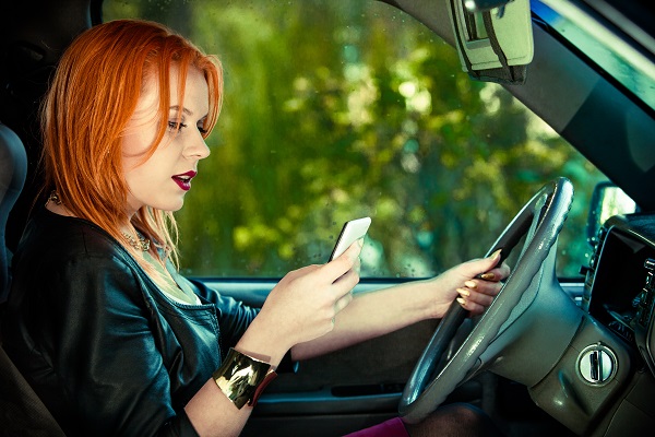 A red haired teenage girl texting on a cell phone while driving a car.